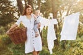 Positive housewife with hangs white clothes to dry. Young mother with her little son is outdoors in the forest. Beautiful sunshine Royalty Free Stock Photo