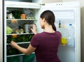 Positive housewife standing near filled fridge