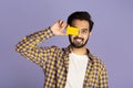 Positive Indian guy closing eye with contactless credit card on violet background