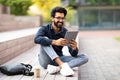 Positive indian guy resting at park after work, using tablet Royalty Free Stock Photo