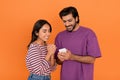 Positive indian young couple using cell phone on orange