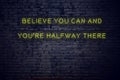 Positive inspiring quote on neon sign against brick wall believe you can and youre halfway there Royalty Free Stock Photo