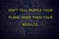 Positive inspiring quote on neon sign against brick wall dont tell people your plans show them your results