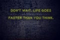 Positive inspiring quote on neon sign against brick wall dont wait life goes faster than you think