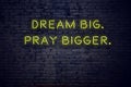 Positive inspiring quote on neon sign against brick wall dream big pray bigger