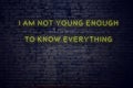 Positive inspiring quote on neon sign against brick wall i am not young enough to know everything