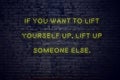 Positive inspiring quote on neon sign against brick wall if you want to lift yourself up lift up someone else