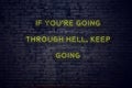 Positive inspiring quote on neon sign against brick wall if youre going through hell keep going