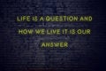 Positive inspiring quote on neon sign against brick wall life is a question and how we live it is our answer