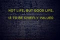 Positive inspiring quote on neon sign against brick wall not life but good life is to be chiefly valued