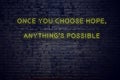 Positive inspiring quote on neon sign against brick wall once you choose hope anythings possible