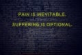 Positive inspiring quote on neon sign against brick wall pain is inevitable suffering is optional