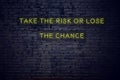 Positive inspiring quote on neon sign against brick wall take the risk or lose the chance