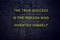 Positive inspiring quote on neon sign against brick wall the true success is the person who invented himself