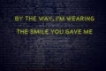 Positive inspiring quote on neon sign against brick wall by the way im wearing the smile you gave me