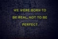 Positive inspiring quote on neon sign against brick wall we were born to be real not to be perfect