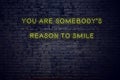 Positive inspiring quote on neon sign against brick wall you are somebodys reason to smile Royalty Free Stock Photo