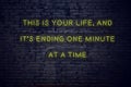 Positive inspiring quote on neon sign against brick wall this is your life and its ending one minute at a time