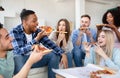 Positive interracial friends having home party, sitting on couch, eating pizza, having fun together indoors Royalty Free Stock Photo