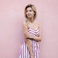 Positive joyful young woman with blond hair with blue beautiful eyes with a cute smile in a trendy summer striped sundress walks Royalty Free Stock Photo