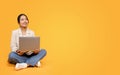 Positive korean millennial lady in suit typing on laptop, sit on floor, look at copy space