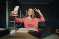 Positive lady sitting at home studying with books and laptop and taking selfie on smartphone camera with a smile on her face Royalty Free Stock Photo