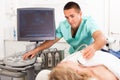 Positive male doctor diagnosing female patient using modern ultrasound scanner in private clinic