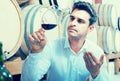 Positive male expert holding glass of red wine in shop