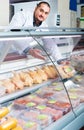 Male shop assistant selling kosher chicken at counter and smiling