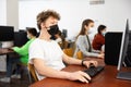 Positive male student wearing face mask working on computer in library. Concept of adult self education during pandemic