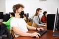 Positive male student wearing face mask working on computer in library. Concept of adult self education during pandemic