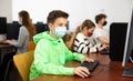 Positive male student wearing face mask working on computer in library. Concept of adult self education during pandemic