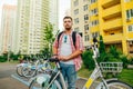 Positive man with a beard and bright casual clothes stands with a bicycle in the background of a row of bicycles and looks at the Royalty Free Stock Photo