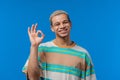 Positive man makes OK hand sign, okay gesture. Happy student guy, correct perfect choice, great deal, blue studio Royalty Free Stock Photo