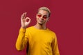 Positive man makes OK hand sign, okay gesture. Happy student guy in yellow, correct perfect choice, great deal, red Royalty Free Stock Photo