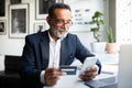 Positive mature european man in suit works, typing on phone, use credit card in modern for good investment