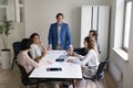 Positive mature male presenter speaking before team at meeting table