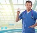 Positive medical doctor showing white vizit card standing on a b