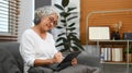 Positive middle age woman browsing wireless internet on digital tablet, relaxing on couch at home Royalty Free Stock Photo