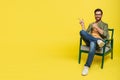 Positive middle aged man in casual sitting in armchair, pointing at copy space, advertising nice product, yellow Royalty Free Stock Photo