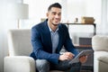 Positive millennial Arab businessman with tablet pc sitting in armchair and smiling at camera in modern office Royalty Free Stock Photo