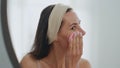 Positive model sponging face looking mirror home closeup. Woman cleaning pores