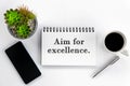 Life or business purpose concept - Aim for excellence. Text on a book with phone, cup of coffee, pen and plant on white background Royalty Free Stock Photo