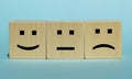 Positive, neutral and negative smiley on wooden cubes on a blue background. Service concept, rating, customer review, satisfaction