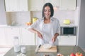 Positive and nice girl stands in kitchen at table and blending together milk with eggs. She likes it. Girl is looking Royalty Free Stock Photo