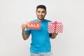 Positive optimistic man with present gift box and sale card, discounts for presents before holidays. Royalty Free Stock Photo