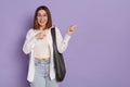 Positive optimistic woman with black bag wearing white shirt and jeans, standing and pointing aside showing copy space for Royalty Free Stock Photo