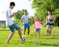 Positive parents with two kids playing soccer together on green field on summer day Royalty Free Stock Photo
