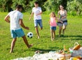 Positive parents with two kids playing soccer together on green field on summer day Royalty Free Stock Photo