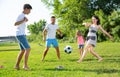 Positive parents with two kids playing soccer together on green field on summer day Royalty Free Stock Photo